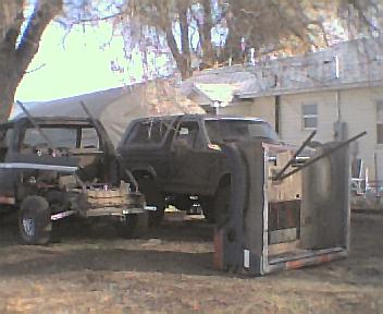 1983 Ford Bronco - Ford Bronco body loaded onto a trailer, next to a pickup truck.