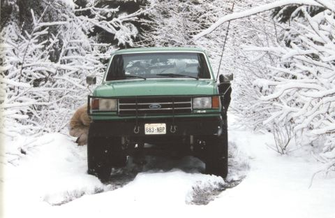 1990 Ford Bronco - A green Ford truck navigates a snowy, wooded path.