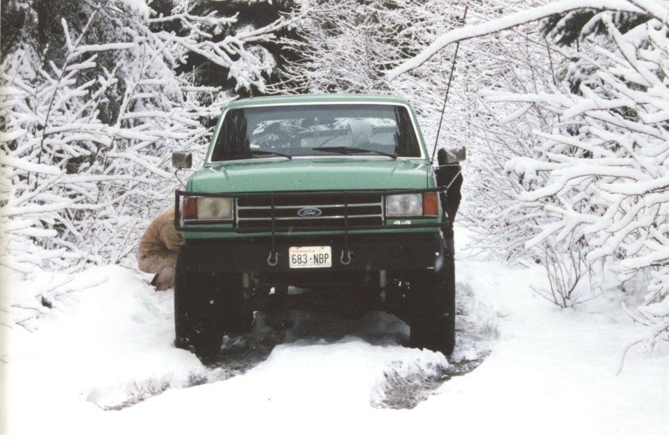 Green lifted Ford Bronco 4x4 head-on in deep snow on a snowy forest trail