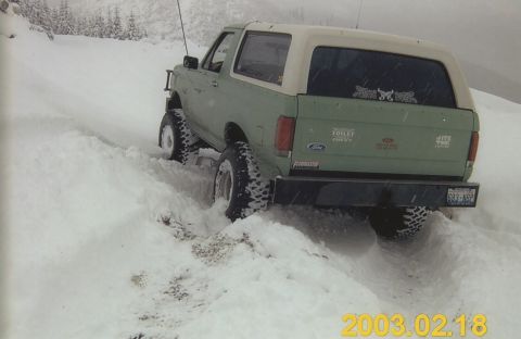 1990 Ford Bronco - A green Ford Bronco with a white top navigates a snowy incline.
