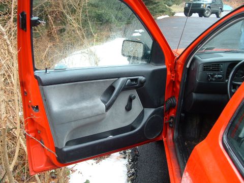 1994 Volkswagen Jetta - The interior door panel of an orange car is visible, with a second vehicle parked outside.