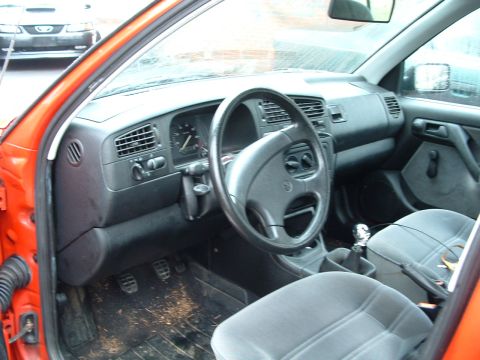 1994 Volkswagen Jetta - The interior of an orange car shows grey seats and a dashboard with a steering wheel and gauges.