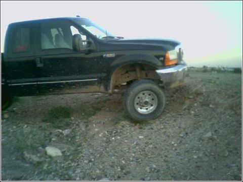 1999 Ford F-250 - A black 1999 Ford F-250 truck is shown from a three-quarter front view on a dirt and gravel lot.