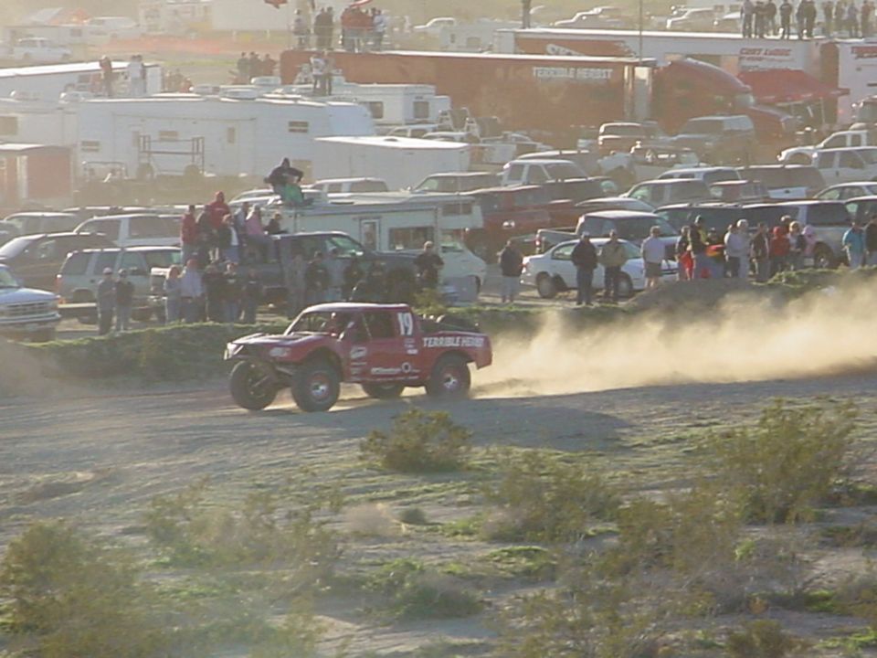 Red off-road truck with number 19, kicking up dust on a dirt track