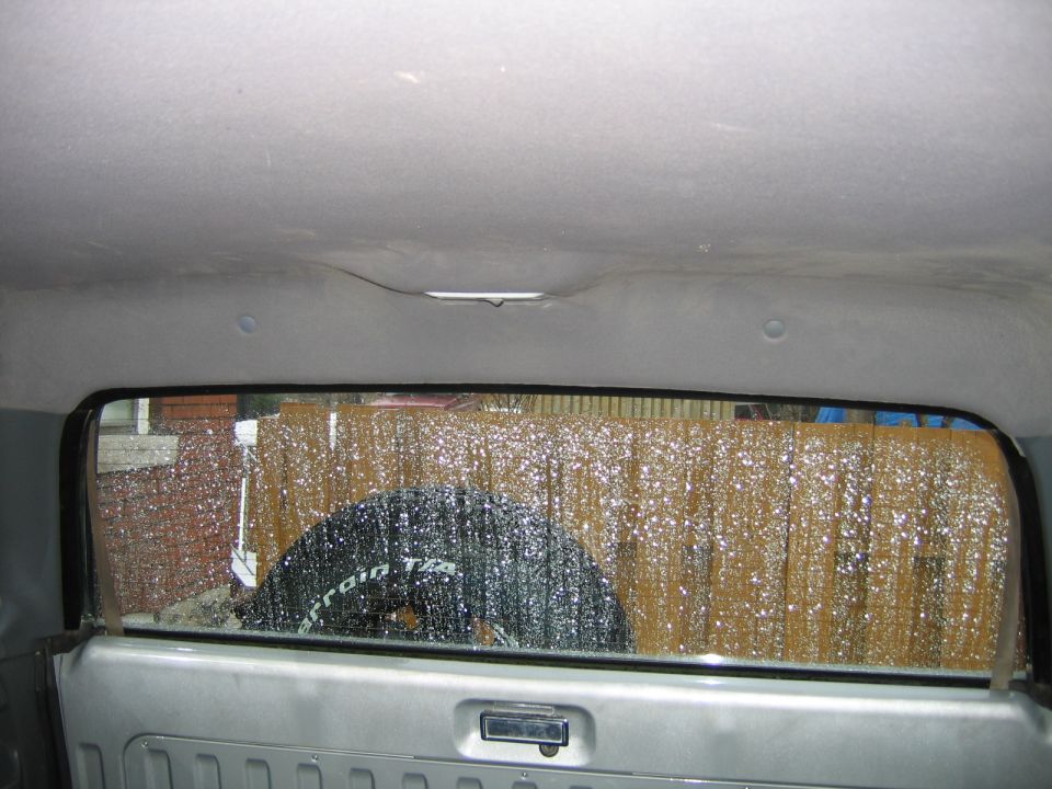 Interior view of a vehicle's rear window showing a spare tire and a fence outside