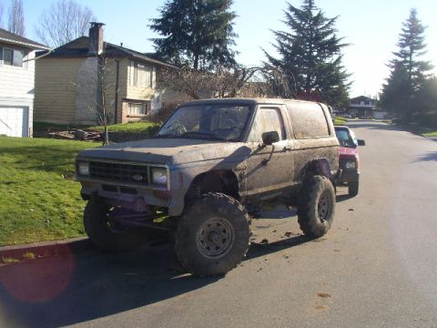 1984 Ford Bronco II - This lifted 1984 Ford Bronco II is covered in mud, suggesting recent off-road use. Another vehicle is visible behind it.
