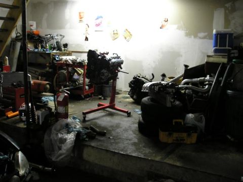 1994 Ford Probe - A cluttered garage space contains an engine on a stand, along with various other automotive parts and equipment.