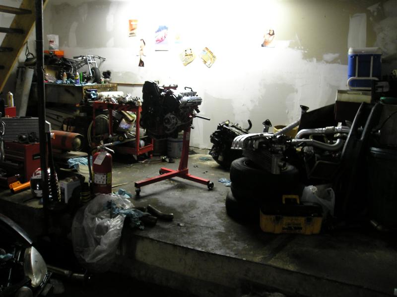 Garage scene with an engine on a stand, spare parts, tires, and tools