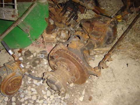 1992 Ford Bronco - Several rusty vehicle axle and differential components are scattered on the ground.