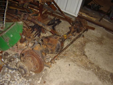 1992 Ford Bronco - Several heavily rusted vehicle axles and components are piled on the ground amidst straw and debris.