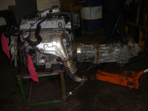 1992 Ford Bronco - Engine and transmission assembly on a stand, with a floor jack visible on the right.