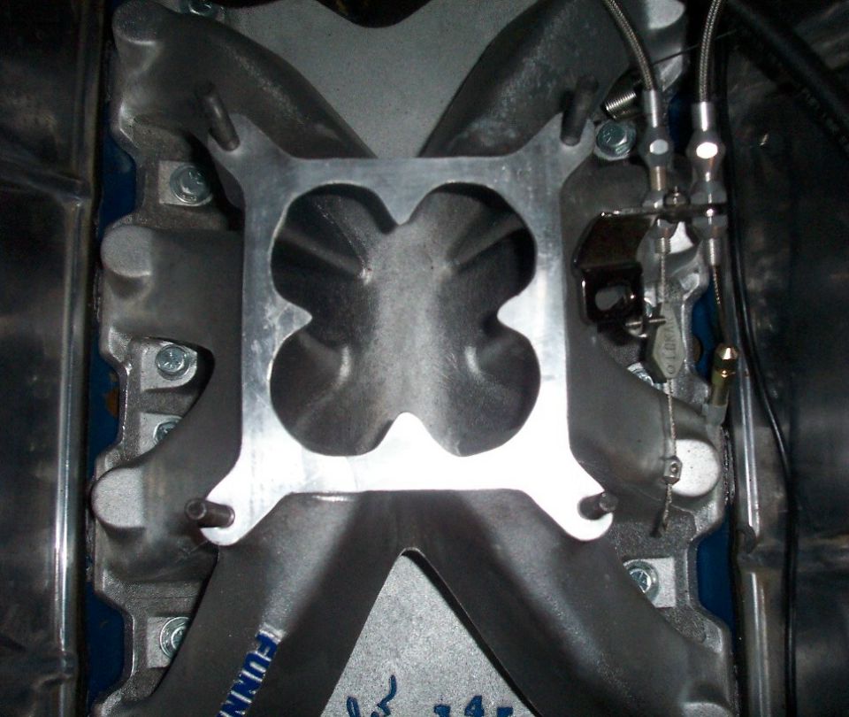 Aluminum intake manifold with a four-hole carb spacer plate mounted on top, viewed from above