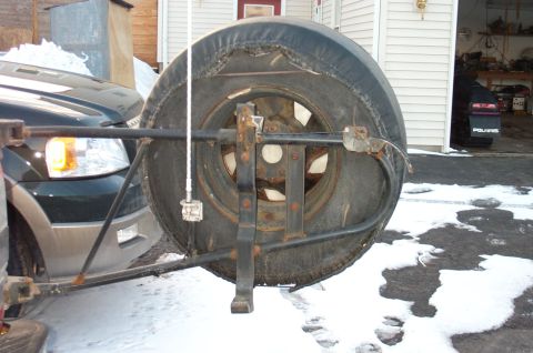 1995 Ford Bronco - A rear-mounted spare tire on a swing-out steel carrier, showing a rusty wheel and worn tire, with a thin white CB or radio antenna mounted…