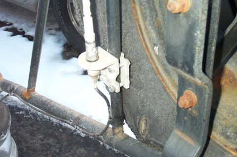 1995 Ford Bronco - Close-up of an antenna base mounted to a rusty black vehicle body panel via an aluminum L-bracket bolted to the fender area, with a white a…