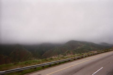 1990 Ford Bronco - Low fog rolling over green hills beside a highway with yellow lane markings and a metal guardrail, shot from a vehicle.