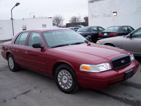 1999 Ford Crown Victoria - Maroon sedan parked in a lot with other vehicles in the background.