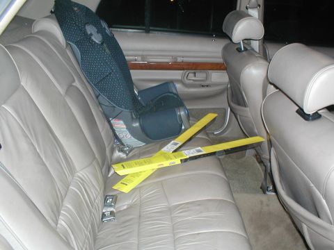 1979 Ford Bronco - The interior of a car shows tan leather seats, a child car seat, and two new windshield wiper packages on the back seat.