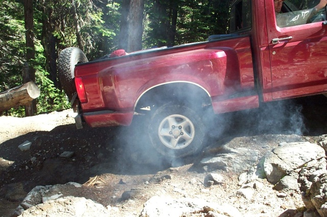 Red 1992 Ford F-150 kicking up dust and smoke while driving over rocks
