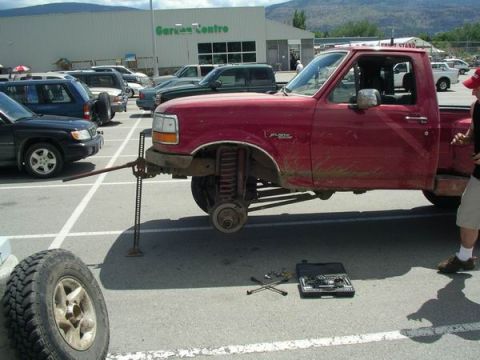 1992 Ford F-150 - A red pickup truck is parked in a lot with its front wheel removed and a jack holding it up.