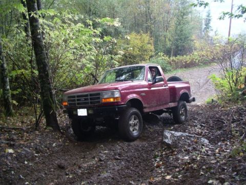 1992 Ford F-150 - Red 1992 Ford F-150 pickup truck navigating a dirt path in a wooded area.