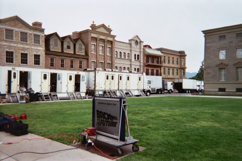 1990 Ford Bronco - Back to the Future cart sign stands before rows of production trailers and trucks on a backlot lawn.