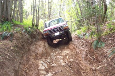 1992 Ford F-150 - Red 1992 Ford F-150 navigating a challenging off-road trail with steep inclines and loose terrain.