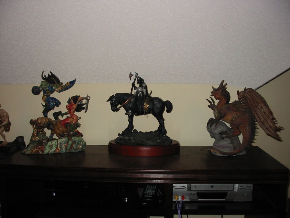 Three fantasy figurines on a dark wooden shelf above electronics
