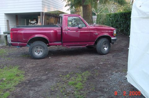 1992 Ford F-150 - A maroon Ford F-150 pickup truck is parked on a dirt lot next to a house and a white tent.