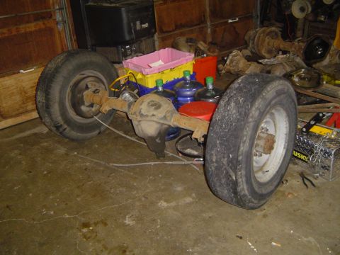 1979 Ford Bronco - A rear axle assembly with tires is stored in a garage, surrounded by various items.