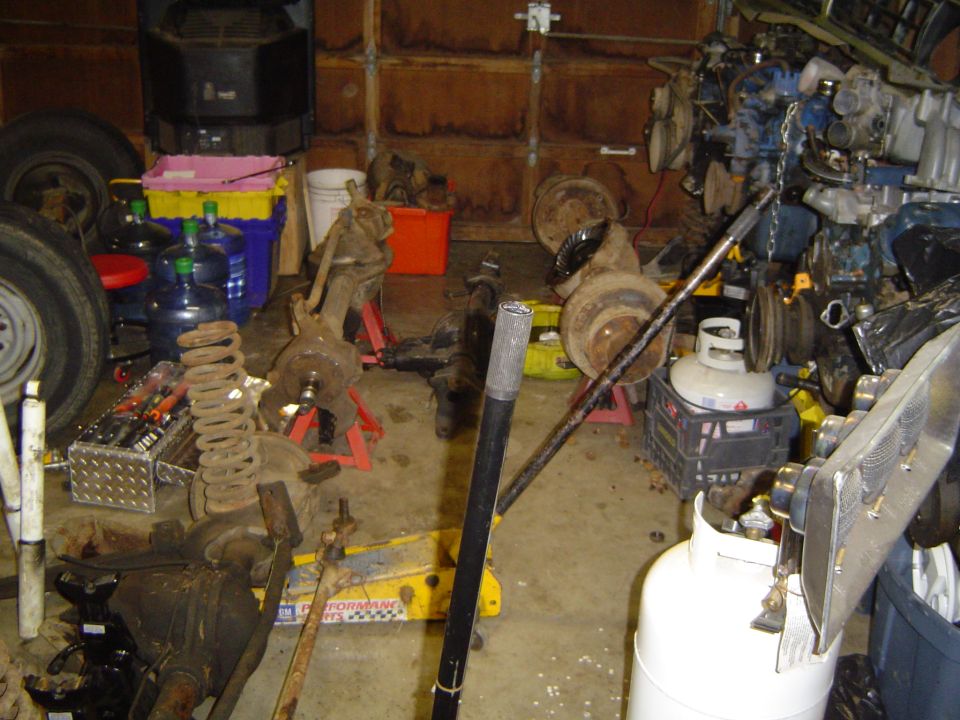 Garage scene with vehicle parts including axles, springs, and an engine block