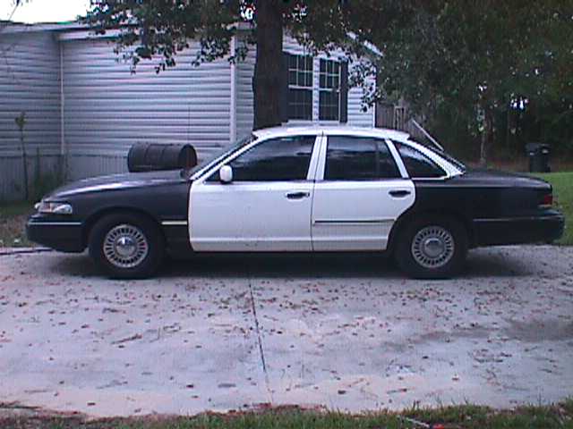 Two-tone black and white Ford Crown Victoria, side view, showing damage on the front fender