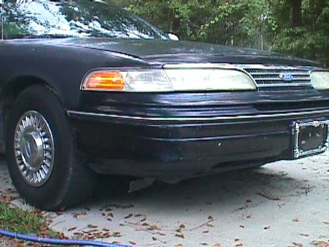 1994 Ford Crown Victoria - The front corner of a black 1992 Ford Crown Victoria is visible, with trees in the background.