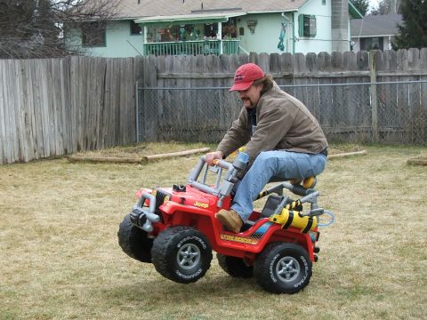 1989 Ford Bronco - A man rides a red toy Jeep labeled "Fire Rescue" in a grassy yard.
