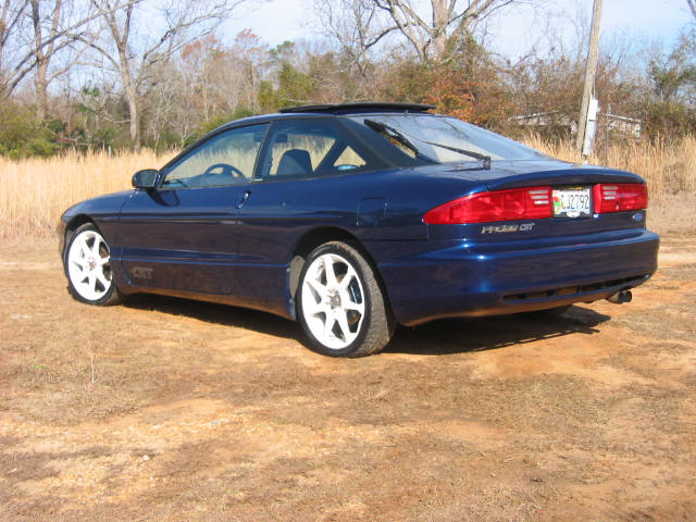 Dark blue Ford Probe coupe rear 3/4 view with white wheels in a dirt field
