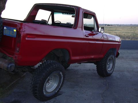 1978 Ford Bronco - A red 1978 Ford Bronco sits parked on pavement, its lifted suspension and large tires suggesting off-road capability.