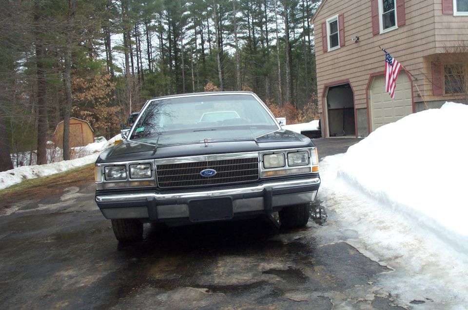 Front view of a dark 1980s Ford Crown Victoria parked in a driveway with snow and ice