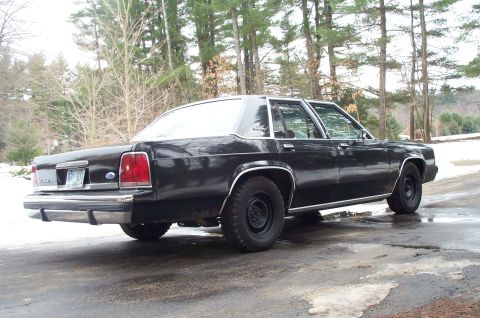 1991 Ford Crown Victoria LTD - A black 1990 Ford Crown Victoria LTD sedan is parked on a wet asphalt surface with snow in the background.