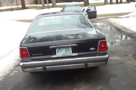 1991 Ford Crown Victoria LTD - Rear view of a black 1991 Ford Crown Victoria LTD, showing its distinctive taillights and chrome bumper. Another car is visible in the back…