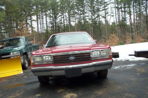 1991 Ford LTD Crown Victoria - A red sedan is parked in front of a wooded area with snow on the ground.