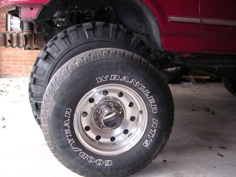 1995 Ford Bronco - Close-up of large Goodyear Wrangler AT/S tires on a red SUV, suggesting off-road modifications.