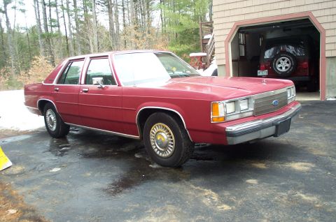 1991 Ford LTD Crown Victoria - A red sedan is parked in front of a garage, where a Jeep is visible inside.