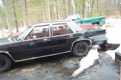 1991 Ford LTD Crown Victoria - A black sedan with a distinctive 1980s body style is parked outdoors, with a green pickup truck in the background.
