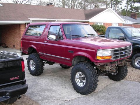 1995 Ford Bronco - A maroon 1995 Ford Bronco is shown with large off-road tires, parked next to another truck.