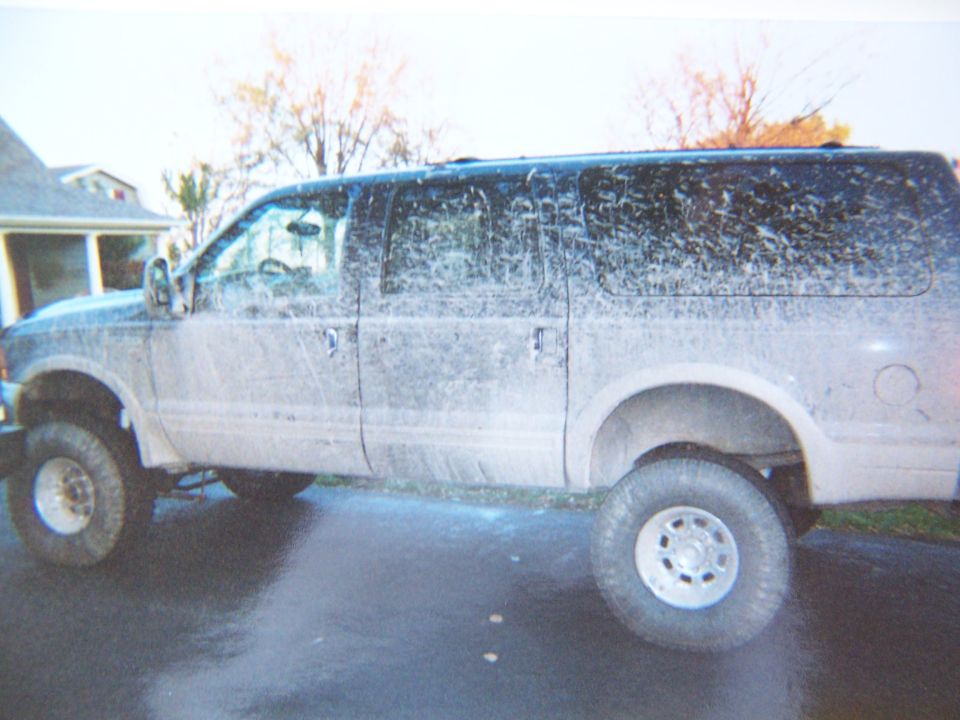 Mud-splattered black 2000 Ford Excursion, side view, parked on a wet driveway