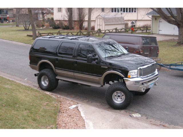 Black lifted full-size SUV with tan cladding on chrome wheels in a driveway