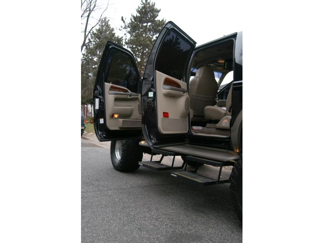 Black lifted SUV with driver-side doors open showing tan interior and deployed power running board steps