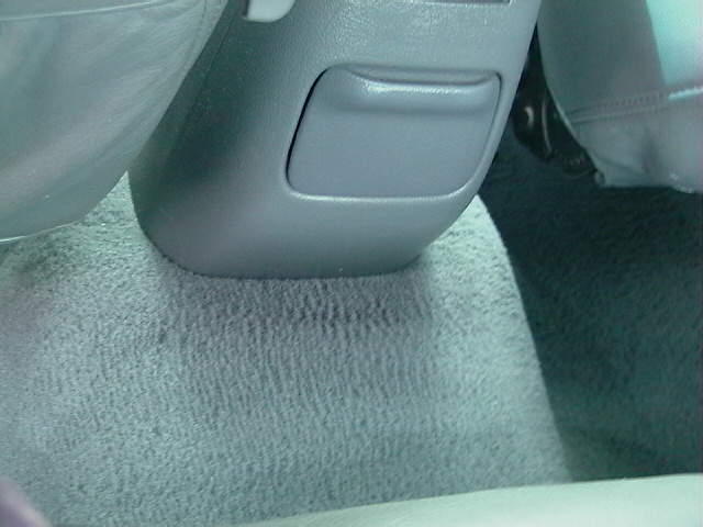Close-up of a gray plastic storage compartment and carpeted floor in a vehicle interior