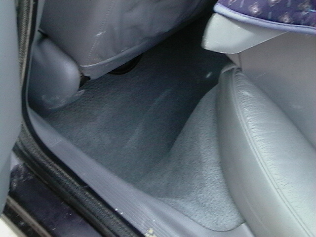 Car interior showing gray carpeted floor and part of a light gray leather seat. A dark fabric seat is visible on the left
