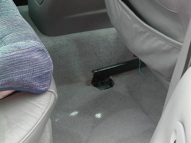 Car interior floor showing gray carpet, seat rails, and part of a seat cushion
