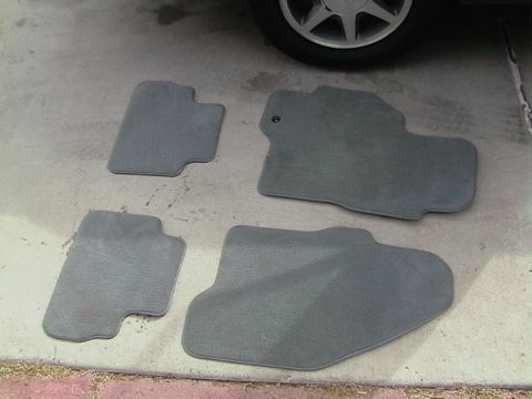 1995 Ford Contour - Four gray carpeted floor mats are shown outside a vehicle, with a portion of a tire and wheel visible.